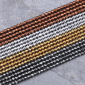 May include: A strand of faceted gemstone beads in four colors: copper, silver, gold, and black. The beads are arranged in rows, with each row a different color.