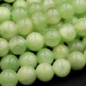 May include: A strand of light green jade beads. The beads are round and smooth, with a slightly translucent appearance.
