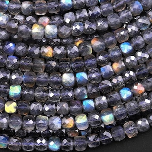 Puede incluir: Una hebra de cuentas de labradorita facetada de color azul oscuro. Las cuentas tienen forma cuadrada y un acabado iridiscente brillante.