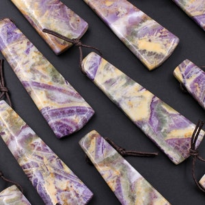 May include: A collection of rectangular pendants with a marbled pattern in shades of purple, yellow, and green. Each pendant has a brown leather cord attached. The pendants are arranged diagonally against a dark background.