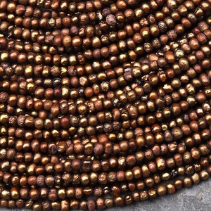 May include: A strand of brown seed beads with a slight iridescent sheen. The beads are small and round, and they are strung together in a long strand.