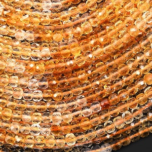 May include: Close-up of a collection of faceted, golden-yellow gemstone beads. The beads are strung together, creating a textured, layered effect. The gemstones have a sparkling, translucent quality, reflecting light.