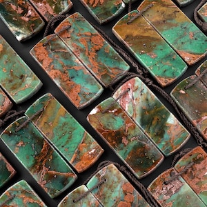 May include: A collection of green and brown gemstone pendants with copper accents. Each pendant is made of two pieces of stone, connected by a brown cord.