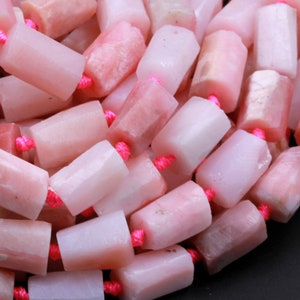 May include: A strand of pink and white gemstone beads, each bead is a rectangular prism shape with a slightly irregular, faceted surface. The beads are strung on a pink thread.