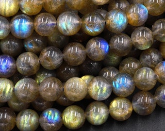 May include: A close-up of a pile of round, iridescent labradorite beads. The beads are a mix of brown, gold, and blue colors. The beads are smooth and polished.