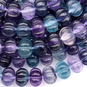 Puede incluir: Una hebra de cuentas de piedras preciosas facetadas de color morado y azul. Las cuentas son redondas y tienen una textura tallada y acanalada.