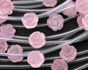 May include: Close-up of rose quartz beads carved into rose shapes. The beads are strung on clear, flexible cords. The rose quartz has a soft pink hue, and the beads are arranged against a black background.