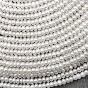 Puede incluir: Una hebra de perlas de agua dulce blancas, cada perla es lisa y redonda. Las perlas están dispuestas en espiral, creando un aspecto hermoso y elegante.