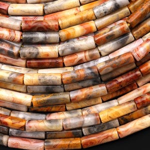 May include: Close-up of a necklace or bracelet made of cylindrical beads. The beads are a mix of colors, including shades of orange, brown, gray, and cream. The beads have a marbled or banded appearance, suggesting they are made of stone or a similar material.