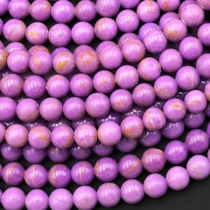 May include: A strand of purple and gold gemstone beads. The beads are round and have a smooth, polished finish.