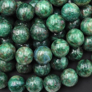 Könnte beinhalten: Nahaufnahme einer Sammlung grüner und brauner Edelsteinperlen. Die Perlen sind rund und haben eine gesprenkelte Optik.