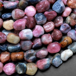 Op de afbeelding: Een streng getrommelde edelsteen kralen in verschillende tinten blauw, roze en bruin. De kralen zijn glad en gepolijst, met een natuurlijke, onregelmatige vorm.