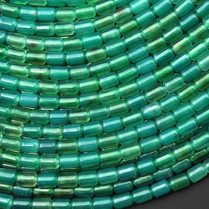 May include: Close-up of a collection of green beads. The beads are cylindrical with rounded edges and a glossy finish. The beads are arranged in a circular pattern, showcasing varying shades of green.