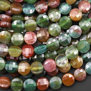 May include: Close-up of a collection of faceted gemstone beads in various colors, including red, green, brown, and yellow. The beads are round and strung together, creating a textured surface. The beads are approximately 10mm in diameter.