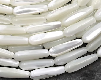 May include: A close-up of a pile of white, pearlescent, teardrop-shaped beads. The beads are smooth and glossy, with a slight iridescent sheen.