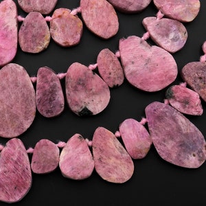 Puede incluir: Una hebra de cuentas de piedras preciosas rosas, cada cuenta tiene una forma irregular única. Las cuentas están enhebradas en un cordón rosa delgado.