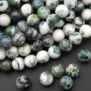 May include: A collection of round, polished beads featuring a white base with marbled green inclusions. The beads are spherical with a smooth, glossy finish and a visible central hole, displaying varied patterns of dark and light green mineral deposits.