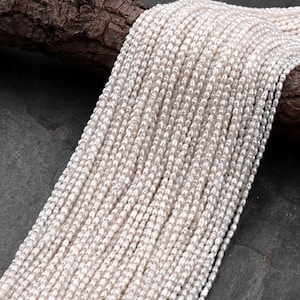 May include: A strand of white freshwater pearls, strung together in a long line. The pearls are small and round, with a smooth, glossy finish.