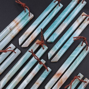 Puede incluir: Una colección de varitas de piedra de ágata turquesa y marrón con lazos de cuero marrón. Las varitas son de diferentes longitudes y tienen un acabado pulido y liso.