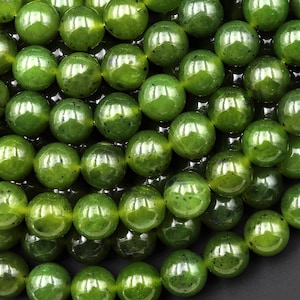 Könnte beinhalten: Eine Schnur grüner Jadeperlen. Die Perlen sind rund und glatt, mit einem glänzenden Finish. Die Perlen sind alle ungefähr gleich groß.