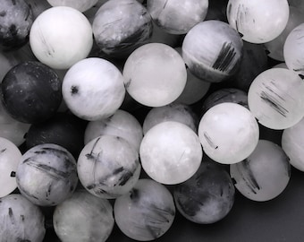 Può includere: Primo piano di una collana di perle rotonde bianche e nere. Le perle sono in pietra naturale e hanno una finitura opaca. Le perle sono infilate su un filo elastico trasparente.