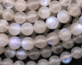 May include: A strand of white moonstone beads with iridescent blue flashes. The beads are round and smooth, and they are arranged in a loose pile.
