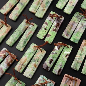 May include: A set of 18 green, brown, and white patterned stone earrings. Each earring is made of two rectangular pieces of stone, tied together with brown string.