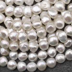 Peut inclure: Gros plan sur de nombreuses perles blanches de forme irrégulière. Les perles ont un éclat nacré et irisé, reflétant la lumière. Les perles sont regroupées, remplissant le cadre, suggérant une collection ou un fil de bijoux. Les perles sont de tailles variables.