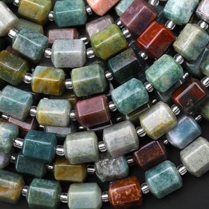 May include: A close-up of a strand of green, brown, and red gemstone beads. The beads are faceted and have a polished finish. The beads are strung on a silver wire.