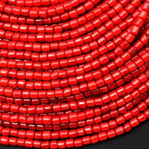 May include: A close-up of a large quantity of bright red coral beads. The beads are small and cylindrical, and they are arranged in a circular pattern.