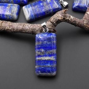 May include: A collection of blue and silver lapis lazuli pendants with a silver bail. The pendants are rectangular and have a striated pattern.