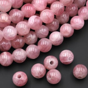 May include: A collection of pink rose quartz beads. The beads are round, with a polished, translucent appearance. The color varies from light to medium pink, with some beads showing internal veining. Ideal for jewelry making.