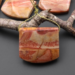 Könnte beinhalten: Eine Sammlung polierter, rechteckiger Steinanhänger in natürlichen Farben wie Rot, Braun und Creme. Jeder Anhänger ist mit einer goldfarbenen Kordel versehen, was darauf hindeutet, dass sie als Schmuck oder Ornamente getragen werden sollen.