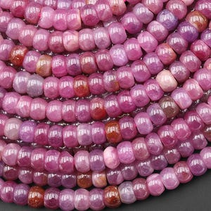 May include: Close-up of a strand of pink and purple gemstone beads. The beads are a mix of shades, from light pink to deep purple, with a polished, glossy finish. The beads are strung together, creating a textured, organic pattern. Ideal for jewelry making.