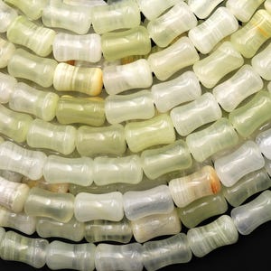 Può includere: Primo piano di una collana di perline a forma di barile verde chiaro e bianco. Le perline hanno una qualità traslucida, con variazioni di colore e opacità. Le perline sono infilate insieme, creando un motivo strutturato e organico.