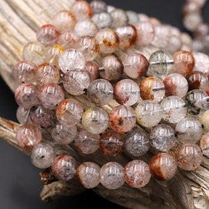 Może przedstawiać: Szereg okrągłych, przezroczystych koralików z wtrąceniami czerwonego, brązowego i zielonego. Korale są nawleczone na przezroczystą nić.