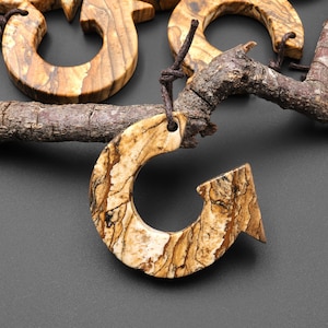 May include: A brown and beige stone pendant shaped like an arrow with a loop at the top. The pendant has a natural, marbled pattern.