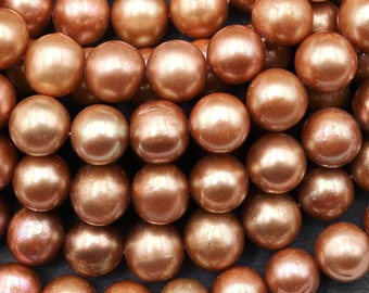 May include: Close-up of numerous, lustrous, copper-colored beads. The spherical beads have a pearlescent sheen, reflecting light and creating highlights. The beads are arranged closely together, filling the frame. Ideal for jewelry making.