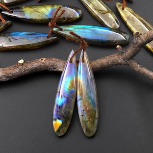 May include: A pair of teardrop-shaped labradorite gemstone earrings with iridescent blue, green, and gold hues. The earrings are suspended from brown cords.