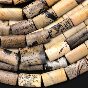 Könnte beinhalten: Eine Schnur aus braunen, schwarzen und weißen gemusterten Steinperlen. Die Perlen sind rechteckig und haben eine glatte, polierte Oberfläche.