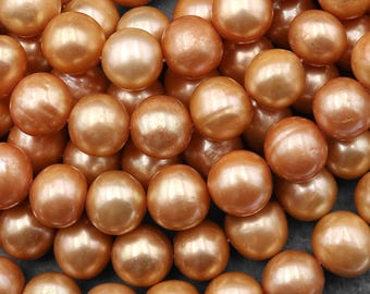 May include: A close-up shot of a pile of lustrous, golden-orange pearls. The spherical beads have a smooth, reflective surface, catching the light and creating highlights. The pearls are scattered, filling the frame and suggesting a large quantity.