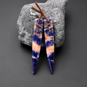 May include: A pair of blue and orange gemstone earrings with a pointed shape. The earrings are attached to brown leather cords.