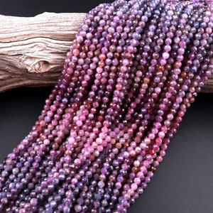 May include: A strand of faceted gemstone beads in shades of pink, purple, and blue. The beads are small and round, and they are strung together on a clear thread.