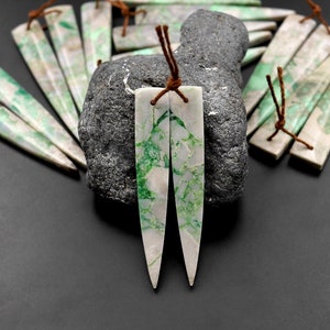 May include: A pair of green and white jade earrings with brown leather cord ties. The earrings are long and narrow, with a pointed tip.