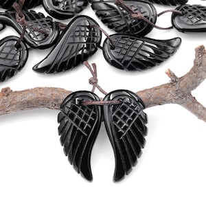May include: Two black onyx angel wing pendants with intricate carvings, hanging from brown cords on a branch.