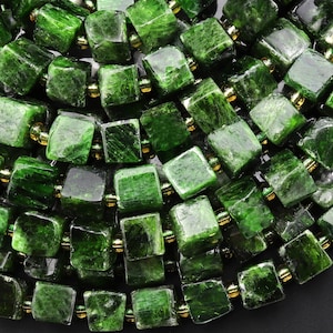 May include: A strand of dark green gemstone beads, each bead is a square shape with a slightly rough texture. The beads are strung on a wire with gold-colored spacers between each bead.