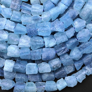 May include: A strand of light blue aquamarine gemstone beads. The beads are faceted and have a rough, natural look. They are strung on a clear elastic cord.