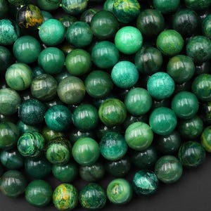 Puede incluir: Un conjunto de cuentas redondas de piedras preciosas verdes pulidas. Las cuentas varían en tonos de verde, con algunos mostrando patrones y texturas únicos. Adecuado para la fabricación de joyas.