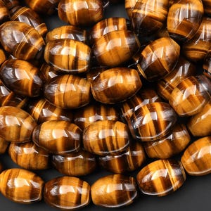 May include: A collection of polished, oval-shaped tiger's eye gemstones. The stones display a rich, golden-brown color with dark brown stripes, creating a chatoyant effect. The gemstones are smooth and appear to be ready for jewelry making.
