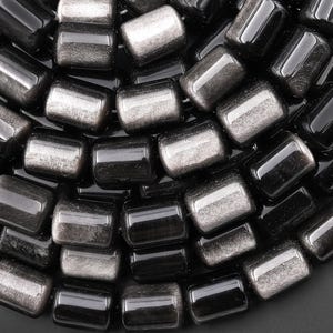 May include: A collection of cylindrical beads arranged in a dense cluster. Each bead features a smooth, glossy black finish on one side and a shimmering, metallic silver-grey texture on the other, creating a high-contrast, reflective appearance.